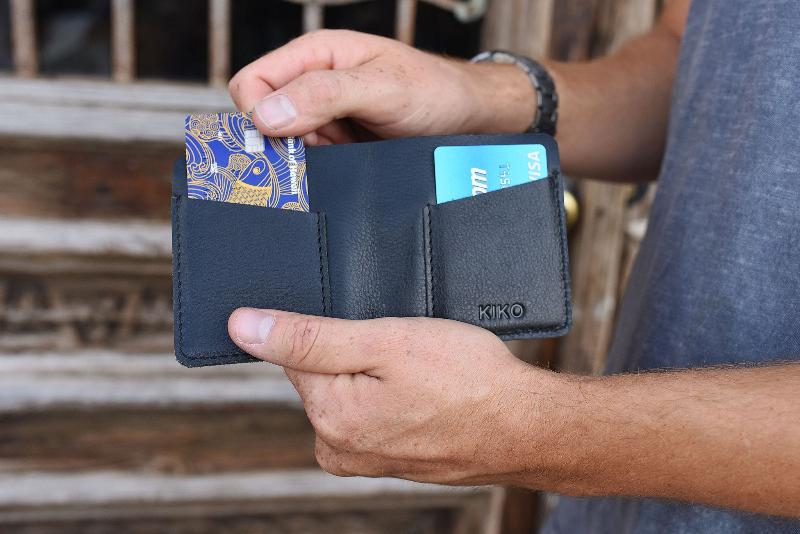 A man is holding a black wallet with a credit card visible, showcasing a casual yet stylish accessory.