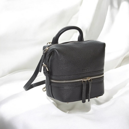 A black leather backpack rests on a clean white surface, showcasing its sleek design and texture.

