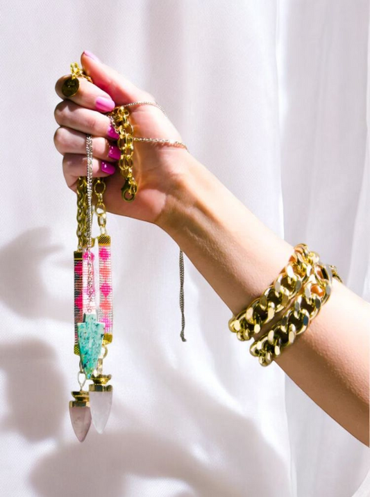 A woman showcasing a shiny gold chain in one hand and a stylish pink bracelet in the other.

