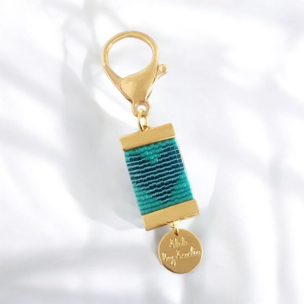 A gold keychain featuring a vibrant blue and green thread, highlighting its unique and stylish design.