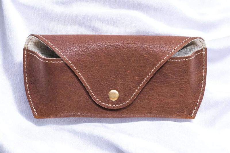 Chic brown leather sunglasses holder with a gold button, ideal for adding a touch of luxury to your everyday carry.