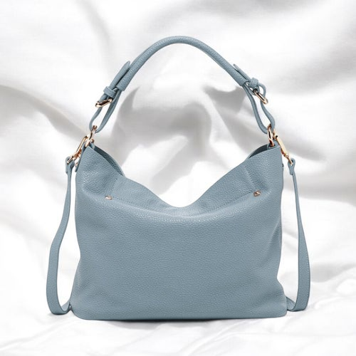 A chic blue leather handbag elegantly rests on a pristine white bed, exuding sophistication and style.