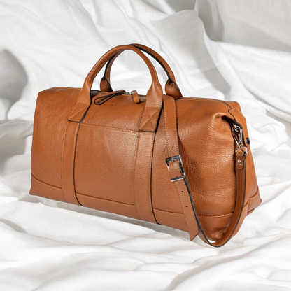 A luxurious tan leather duffel bag elegantly placed on a pristine white bed, exuding sophistication and style.