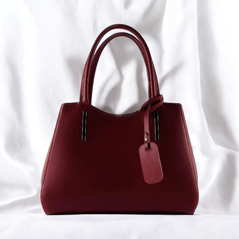 A luxurious burgundy leather handbag elegantly displayed against a pristine white background, showcasing its exquisite craftsmanship.