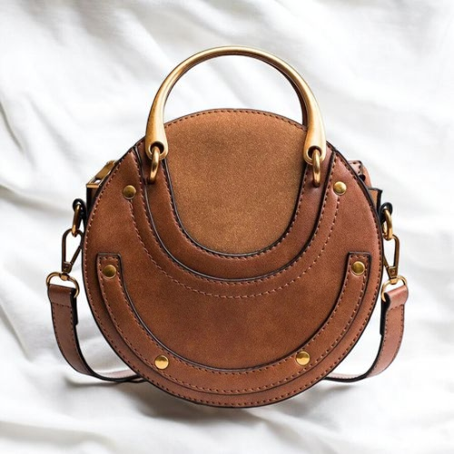 A round brown leather purse rests elegantly on a pristine white bedspread.