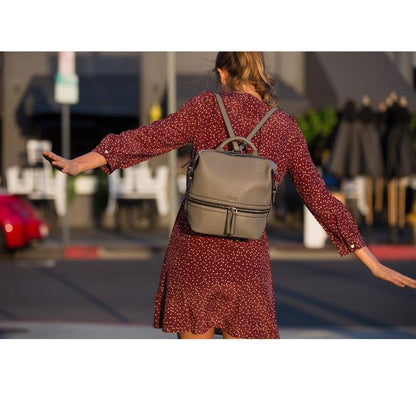 A woman in a dress and backpack crosses the street, showcasing a blend of style and practicality in her journey.