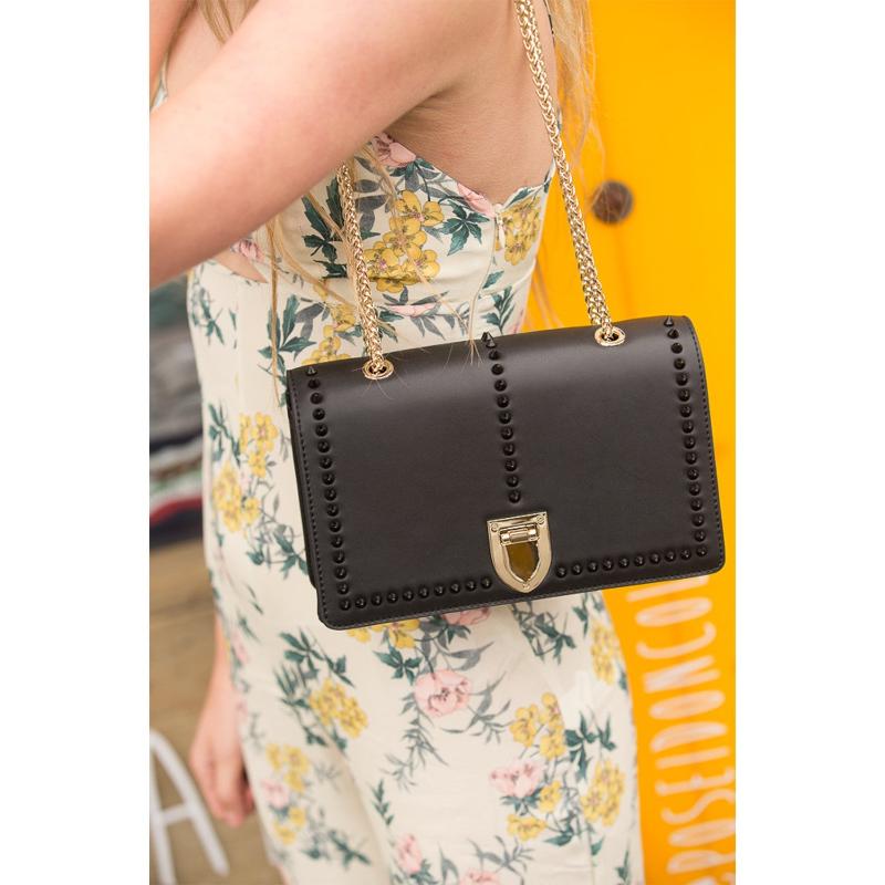 A woman in a floral dress smiles while holding a stylish black purse.