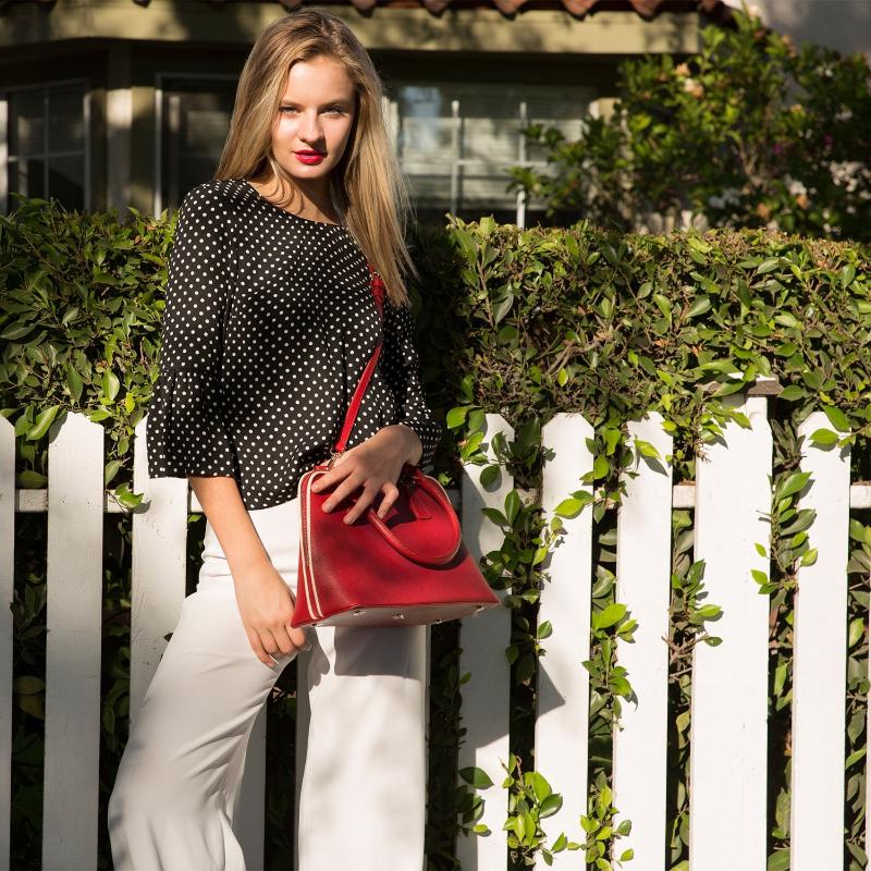 Woman with a white pants and a black shirt holding a red fashion bag.