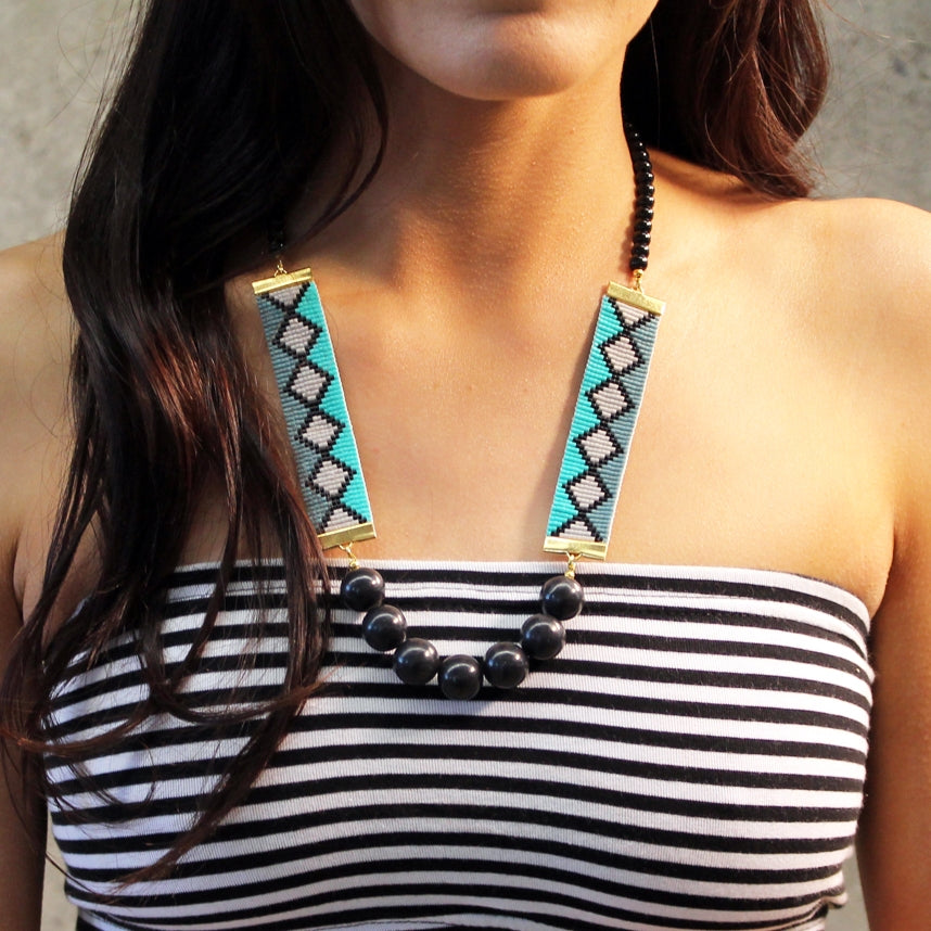 A stylish woman in a striped top adorned with a chic geometric necklace, exuding elegance and modern flair.