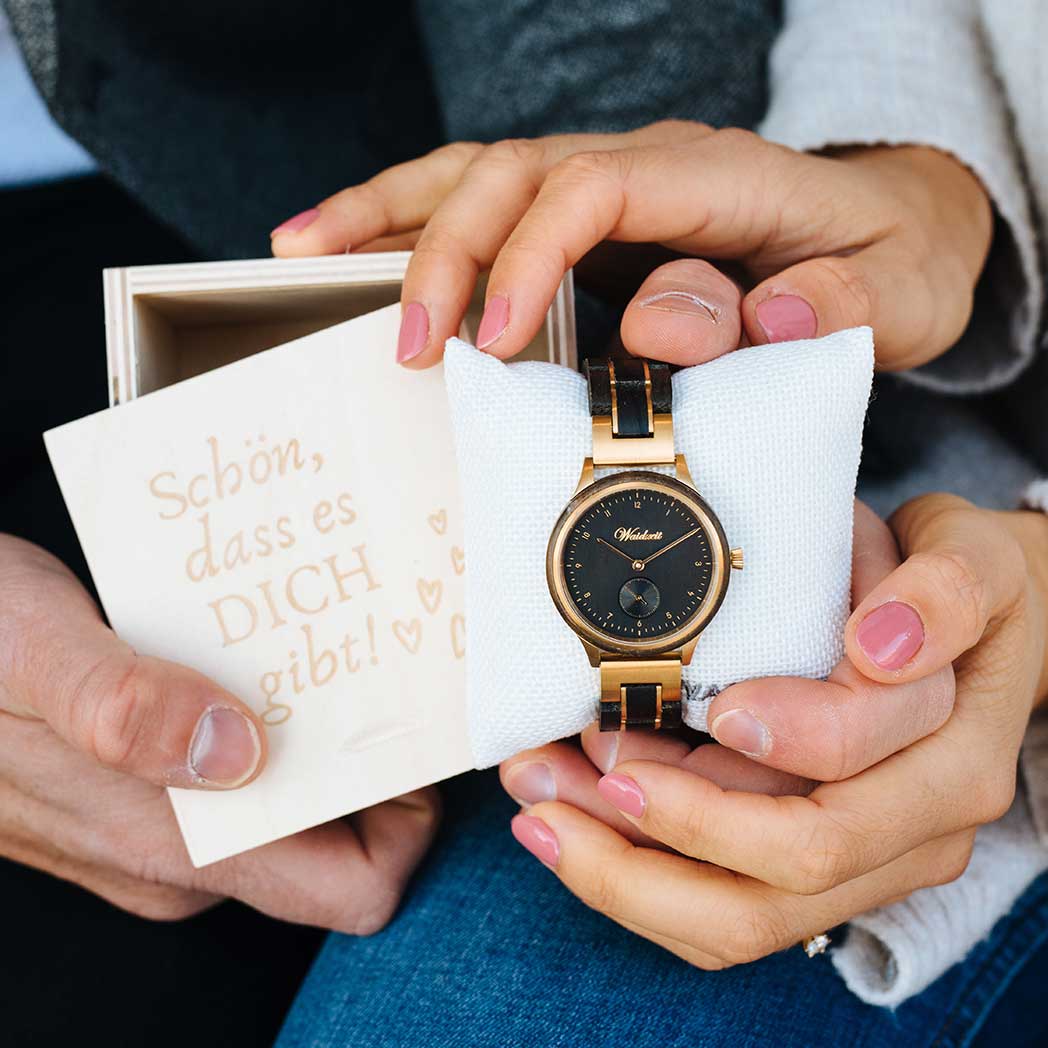 A man and woman are holding a watch together, showcasing it in their hands with smiles on their faces.