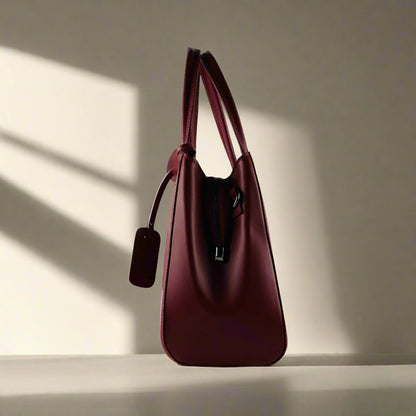 A luxurious burgundy leather handbag elegantly displayed against a pristine white background, showcasing its exquisite craftsmanship.