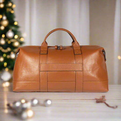 A luxurious tan leather duffel bag elegantly placed on a pristine white bed, exuding sophistication and style.