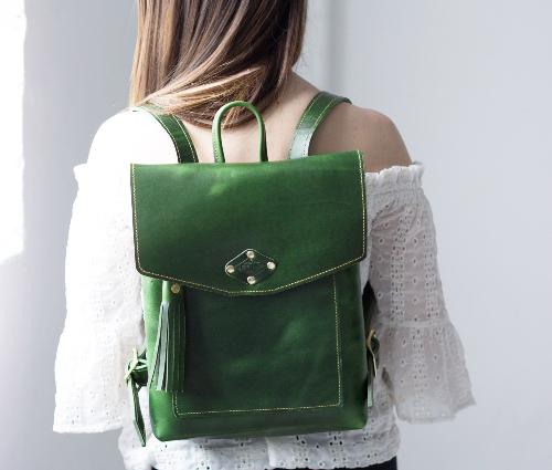 A woman with a green backpack featuring a gold buckle, standing confidently outdoors.