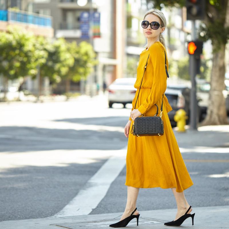 This woman in a yellow dress is holding a small black purse. Her look is elegant and sophisticated.