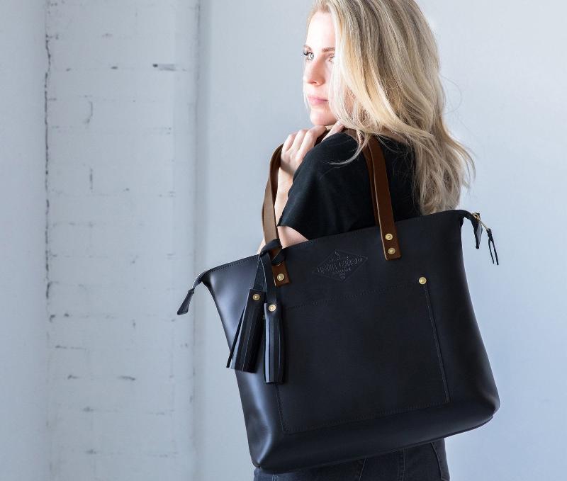 Elegant black leather tote bag featuring a sophisticated brown handle, perfect for a chic and stylish look.