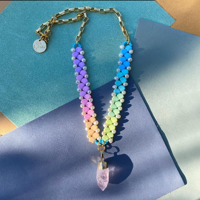 A vibrant rainbow-colored necklace featuring a striking crystal point at its center.