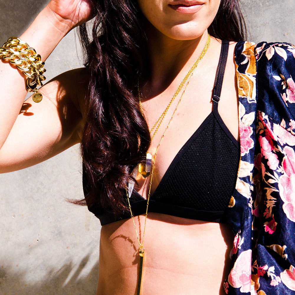 A woman wearing a bikini top and floral jacket, accentuated by a prominent pink necklace.