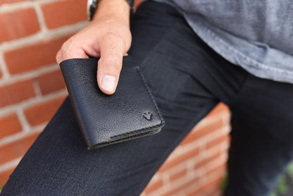 A man, is holding a black wallet with a credit card visible, showcasing a casual yet stylish accessory.