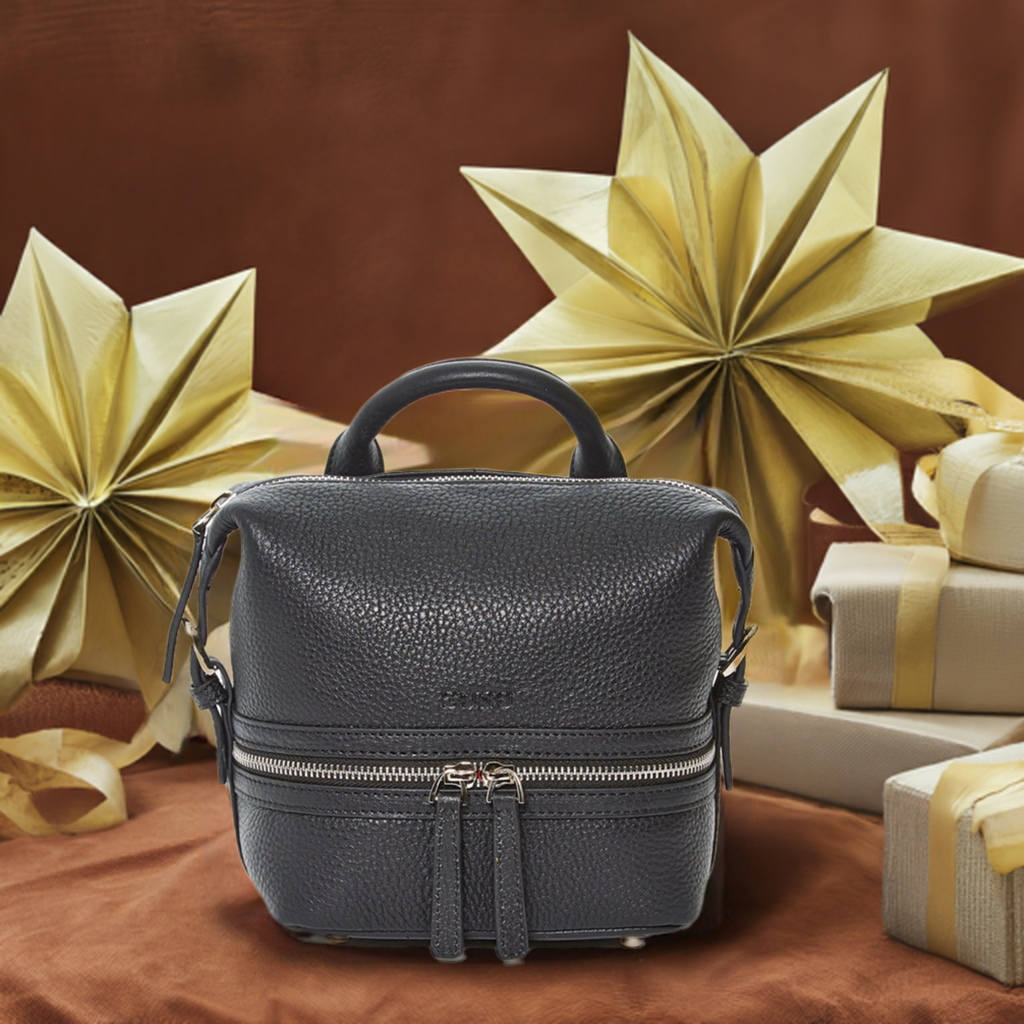 A black small leather backpack rests on a table with holiday gifts, showcasing its sleek design and texture.

